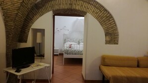 A cozy room with a television on a small table, a bed with a floral bedspread, and a yellow sofa. - Svegliarsi nei Borghi - La Patronale (Troia)