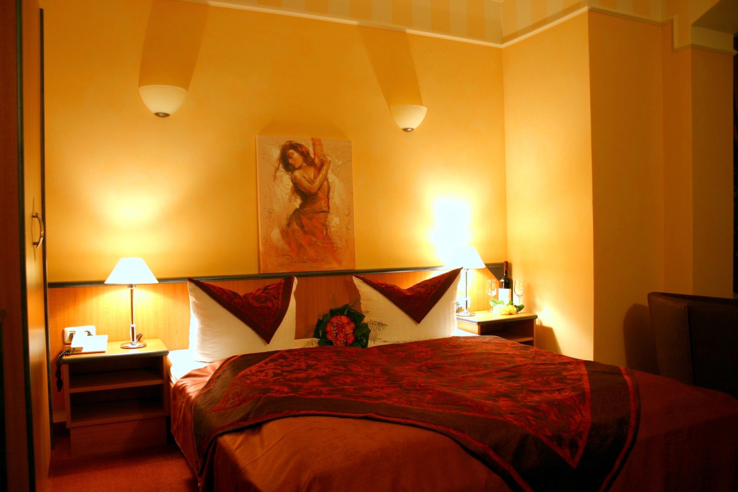 Hotelkamer met een bed, twee bedlampjes, een nachtkastje, een schilderij aan de muur en een tafeltje met een vaas.
