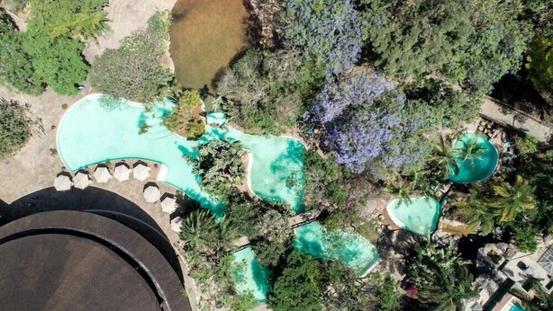An aerial view of a resort with multiple swimming pools surrounded by lush greenery and palm trees. - SAFARI PARK HOTEL (NAIROBI)