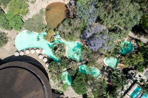 An aerial view of a resort with multiple swimming pools surrounded by lush greenery and palm trees.