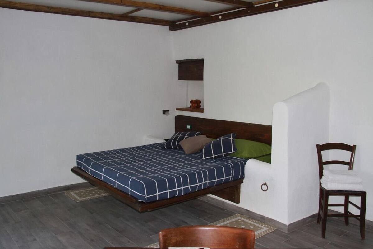 A bedroom with a bed, a chair, a small shelf, and a mirror.