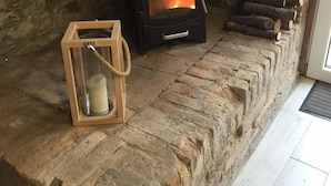 A stone fireplace with a black stove, a wooden lantern, and logs stored beside it. - LeAmorine White House B&B (Predappio)