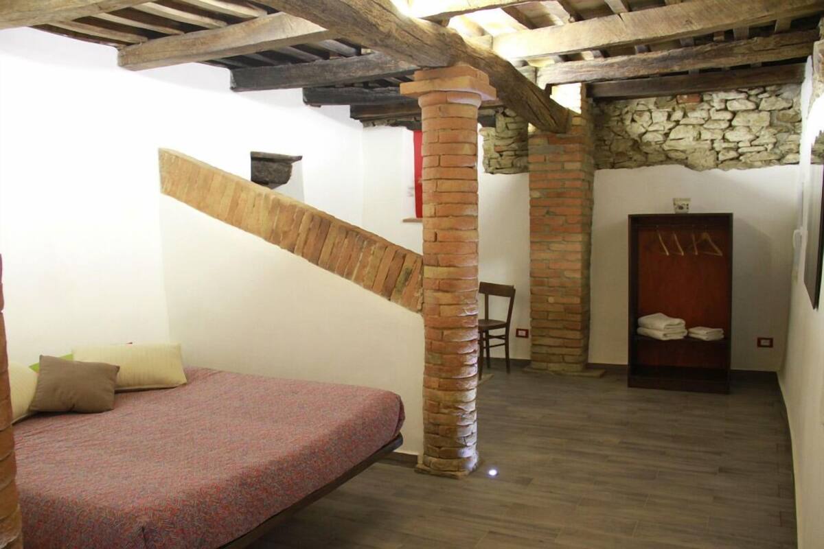 A bedroom with a wooden bed, a brick column, a stone wall, and a wooden door.