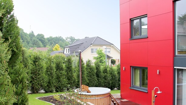 A modern red building with a wooden deck, a hot tub, and a landscaped garden with a curved path. - Holiday directly on the Reinhardswald (Trendelburg)