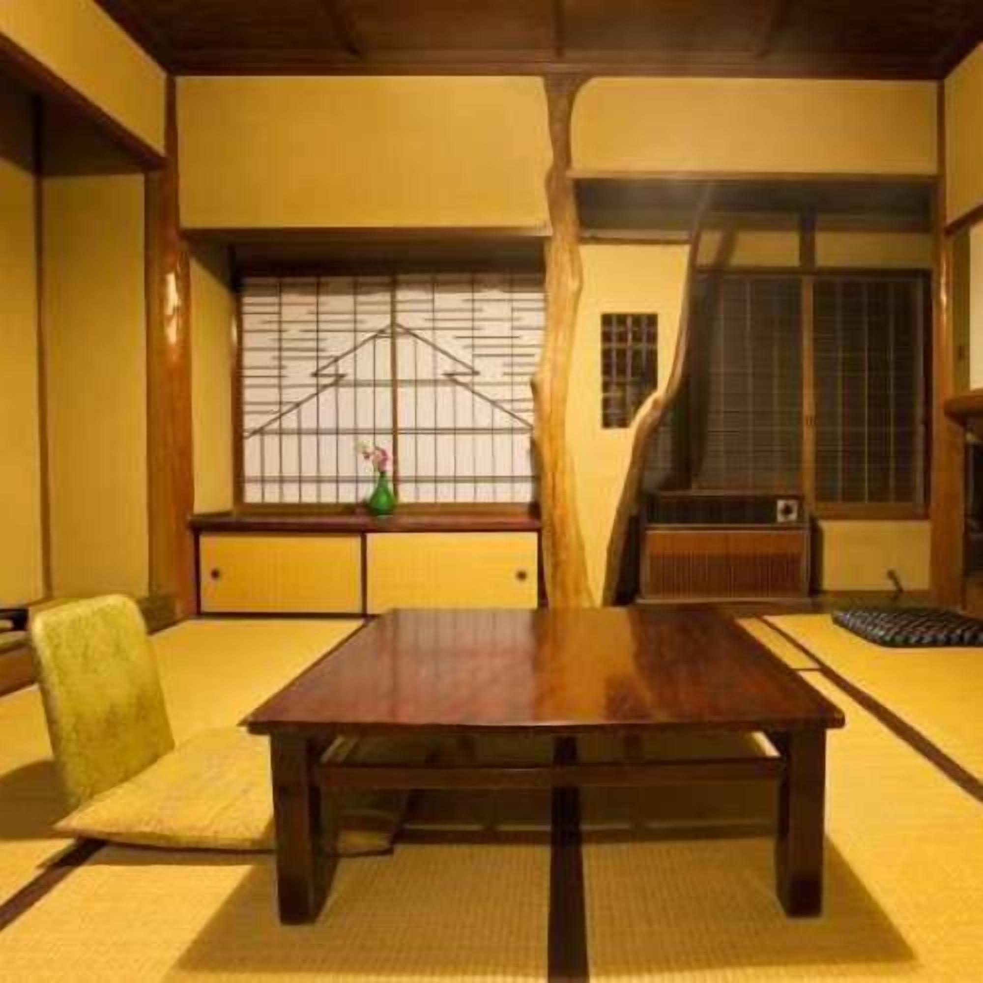 Habitació japonesa tradicional amb tatami, una taula baixa, una cadira verda i una finestra amb vista a l'exterior.