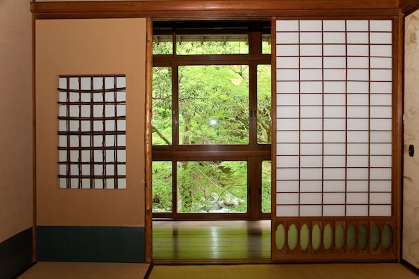 A traditional Japanese room with tatami flooring, a shoji screen door, and a view of a lush garden. - Fukuzumiro (Hakone)
