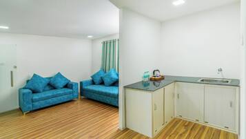 Una habitación con dos sofás azules, una pequeña cocina con un fregadero y suelo de madera.