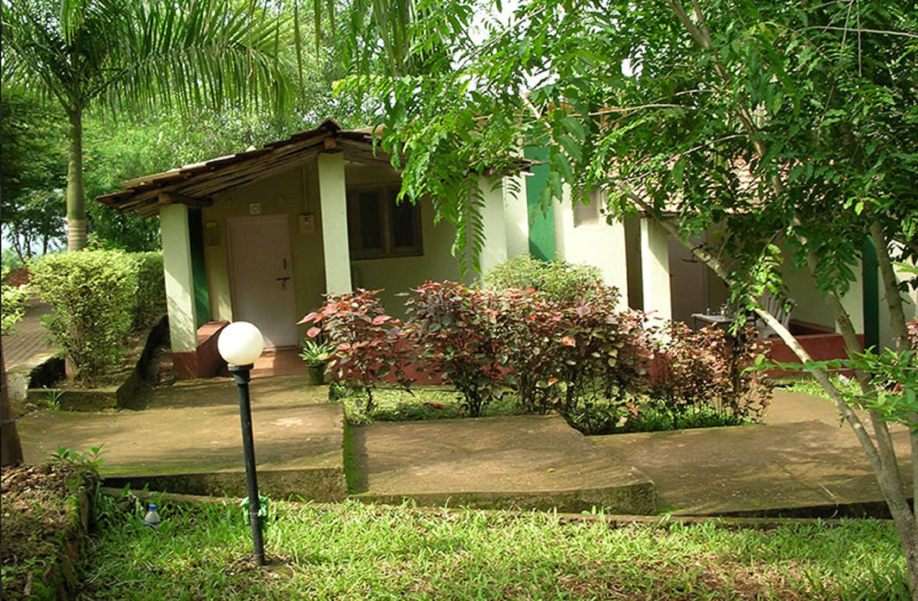 A small, single-story building with a sloped roof, surrounded by lush greenery and a well-maintained garden.