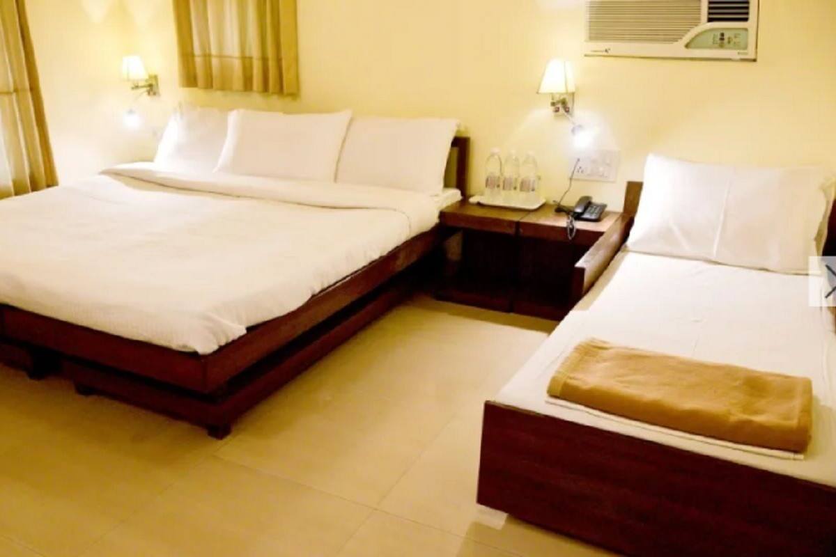 Habitación de hotel con dos camas, una mesita de noche con lámpara y un aire acondicionado de pared.