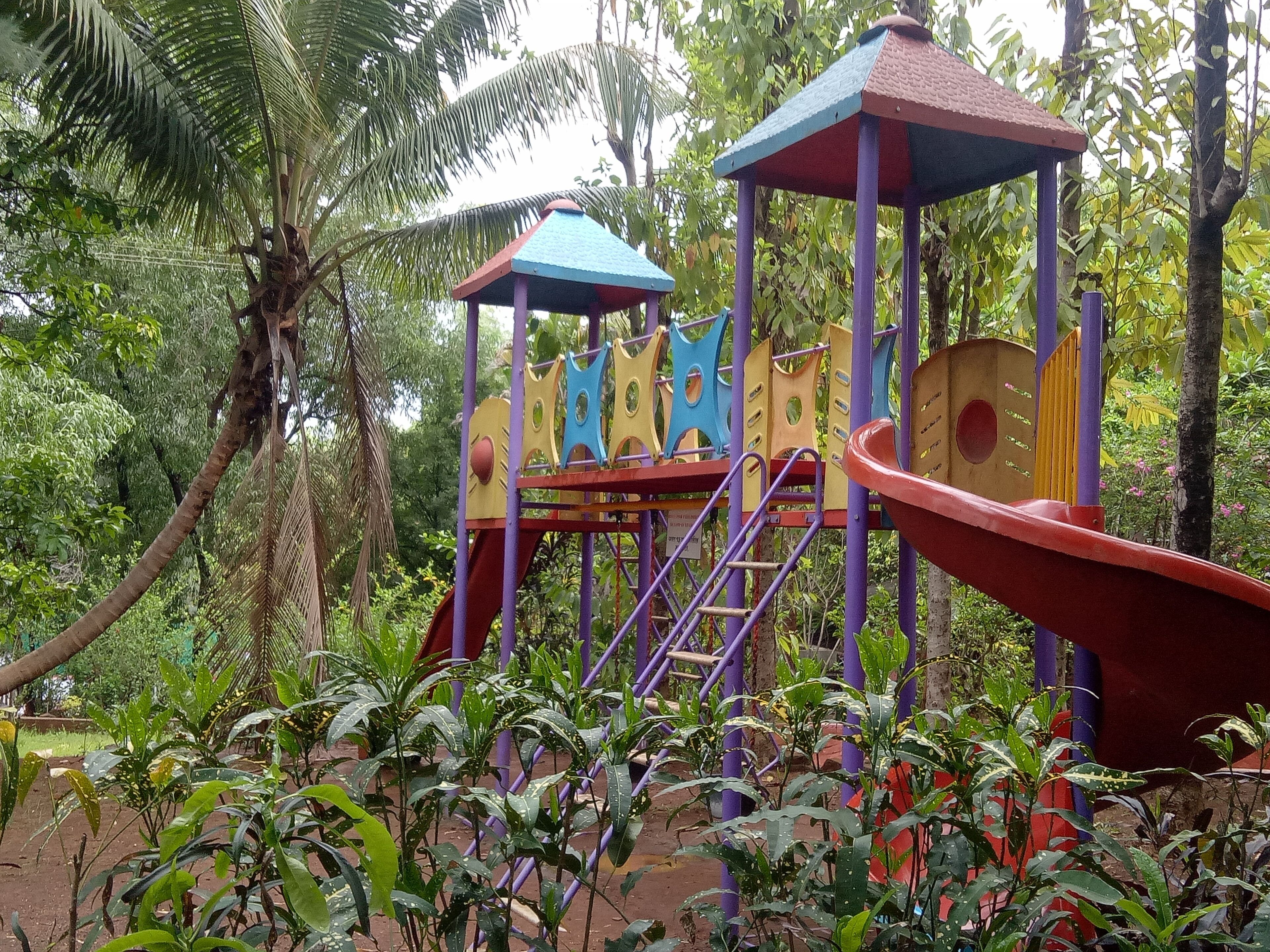 Un parque infantil con estructuras de juego y toboganes coloridos, rodeado de abundante vegetación.