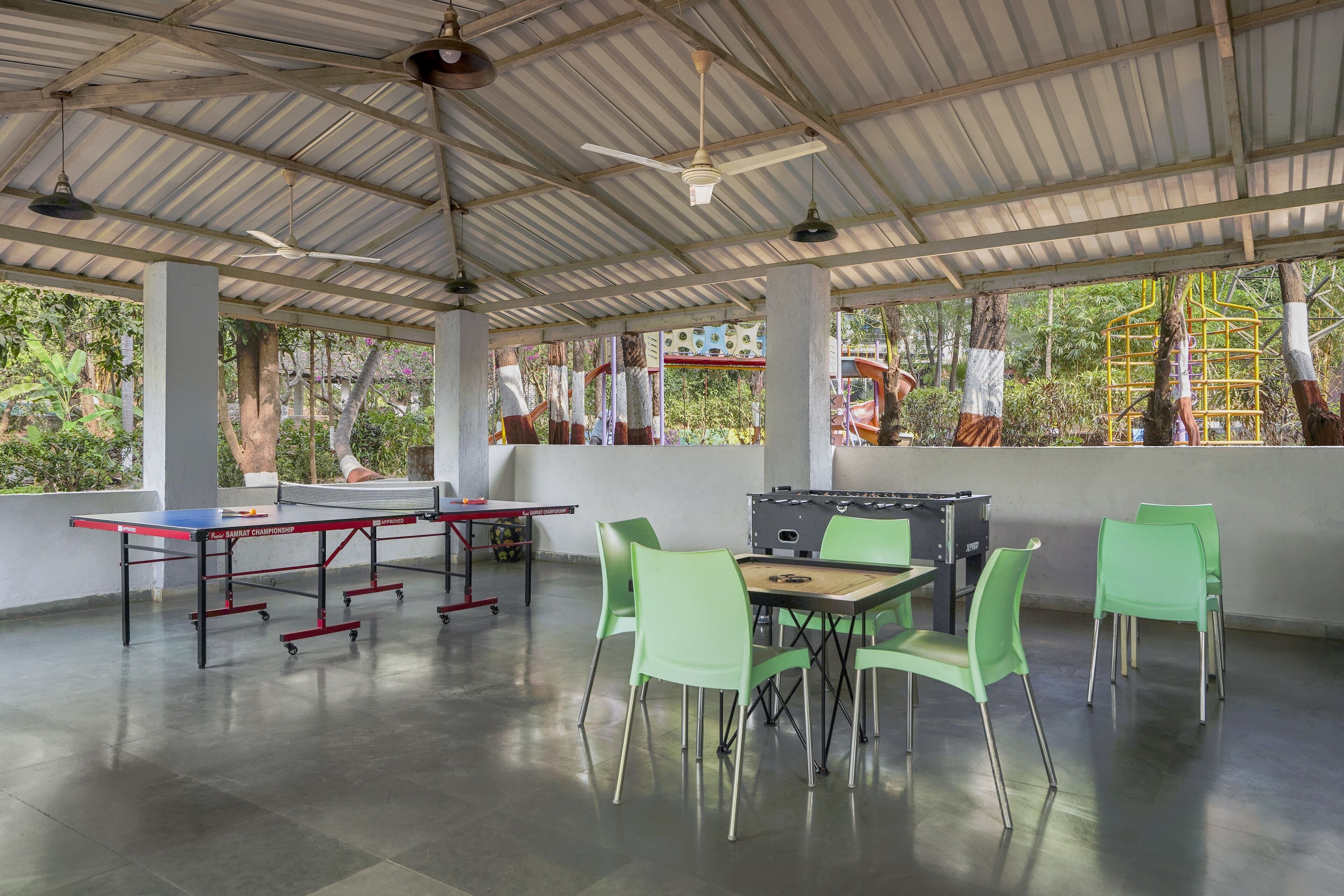 Un espacio al aire libre techado con mesa de ping pong, mesa de fútbol y sillas verdes.
