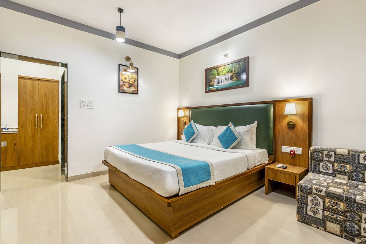 Un dormitorio moderno con una cama de madera, un cabecero tapizado en verde, una mesita de noche con lámpara y un sillón con estampado.