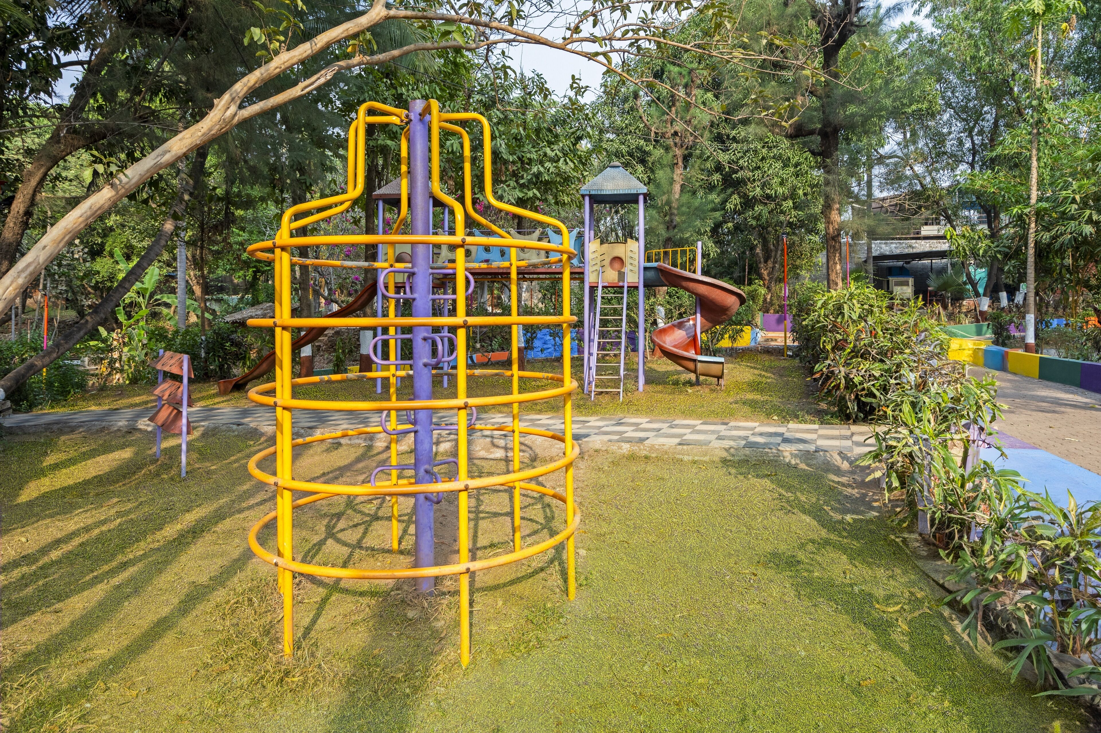 Une aire de jeux avec une structure d’escalade jaune en forme de spirale, des toboggans et un petit abri.
