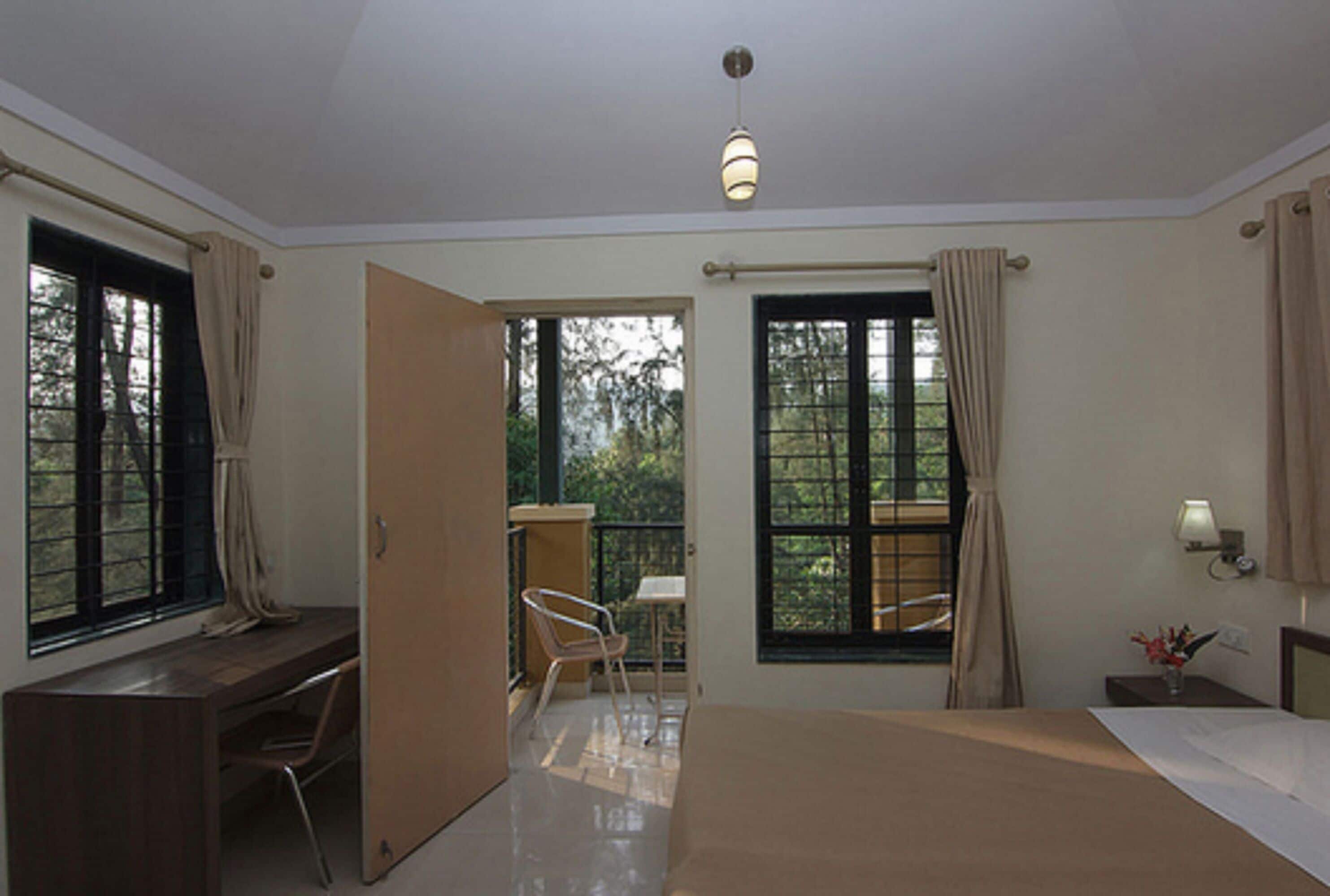 Une chambre à coucher avec un lit, un bureau et une chaise. Il y a une fenêtre avec des rideaux et une vue sur les arbres.