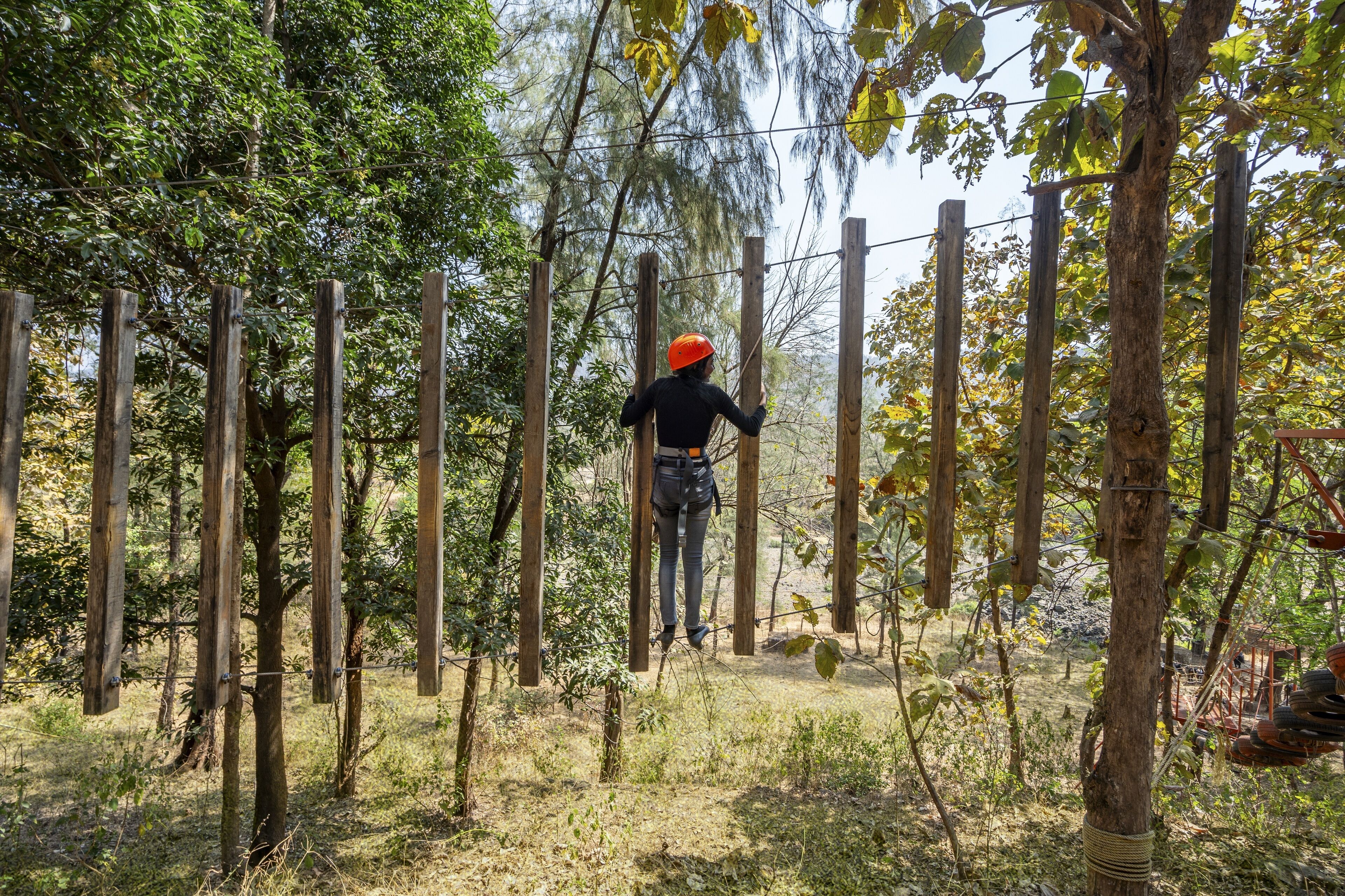 A person navigating a rope course in a wooded area with wooden poles and ropes.