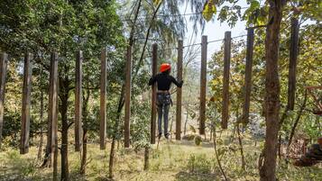 A person navigating a rope course in a wooded area with wooden poles and ropes.
