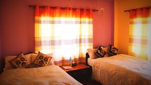 Habitación de hotel con dos camas, una mesita de noche y una ventana con cortinas estampadas.