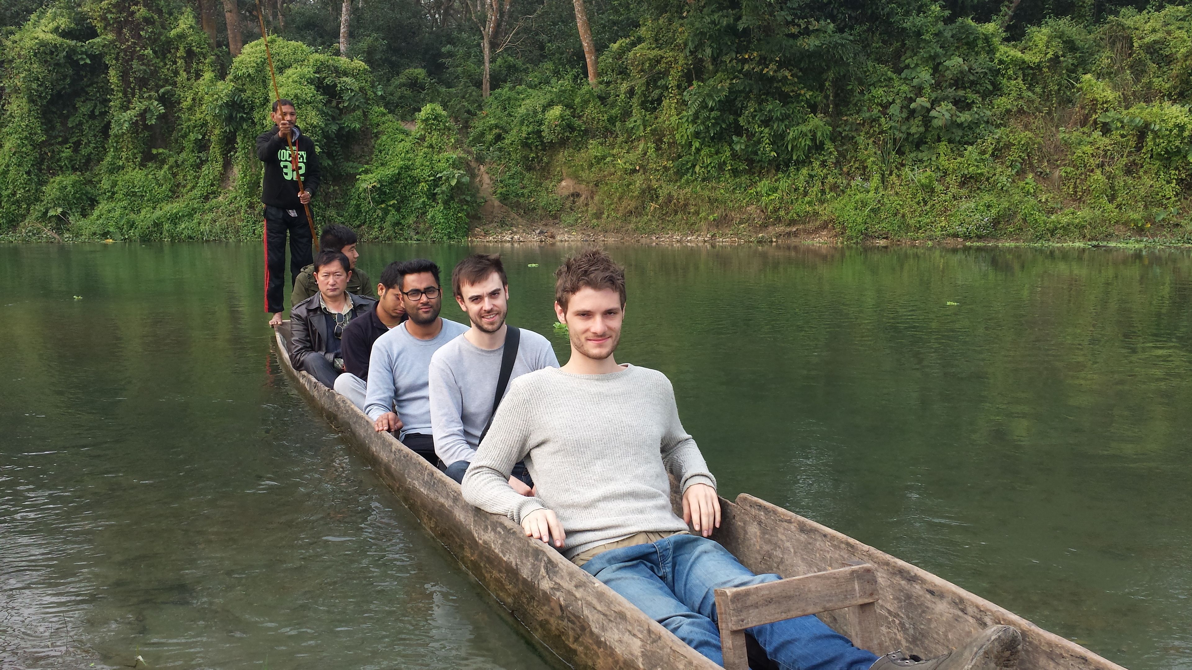 A group of people in a wooden boat on a calm river surrounded by dense greenery.