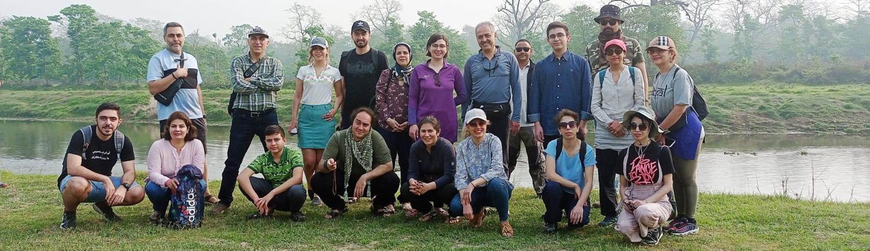A group of people gathered outdoors near a body of water, with trees in the background.