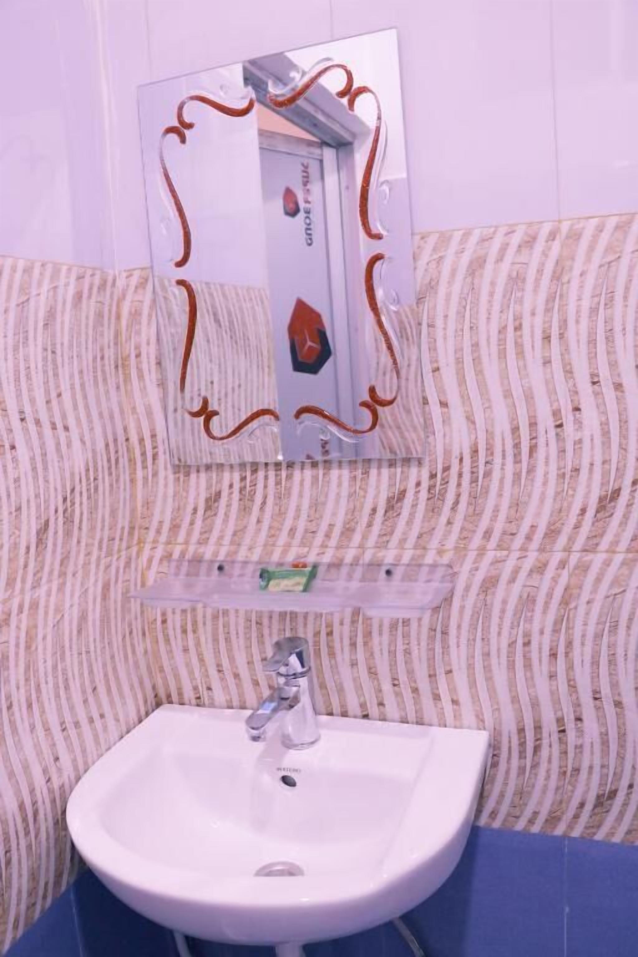Une salle de bain avec un lavabo blanc, un miroir doté d’un cadre décoratif et un papier peint à rayures.