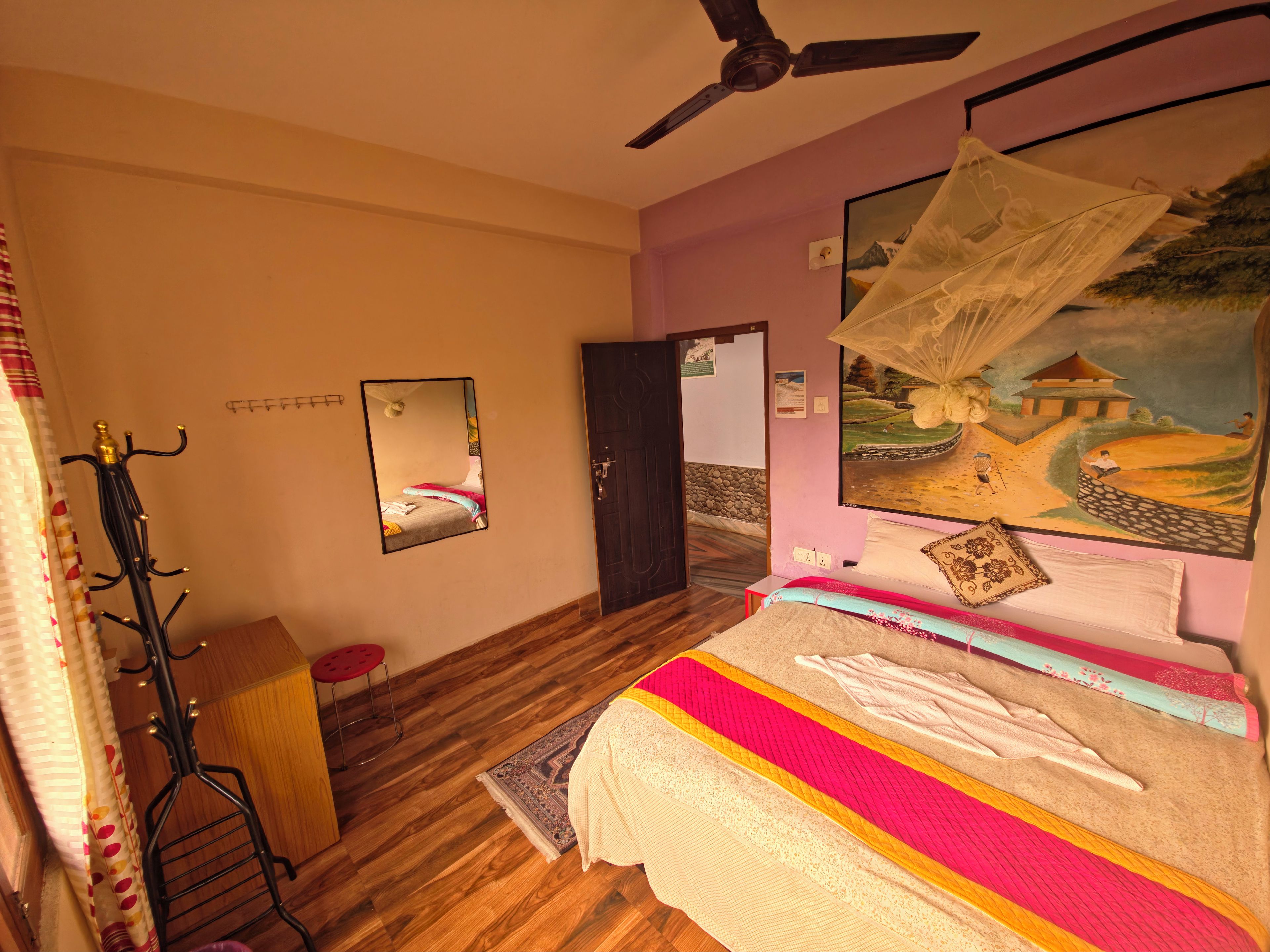 Une chambre à coucher avec un lit, un ventilateur de plafond, un tableau, un porte-manteau et une porte.
