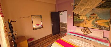 Une chambre à coucher avec un lit, un ventilateur de plafond, un tableau, un porte-manteau et une porte.
