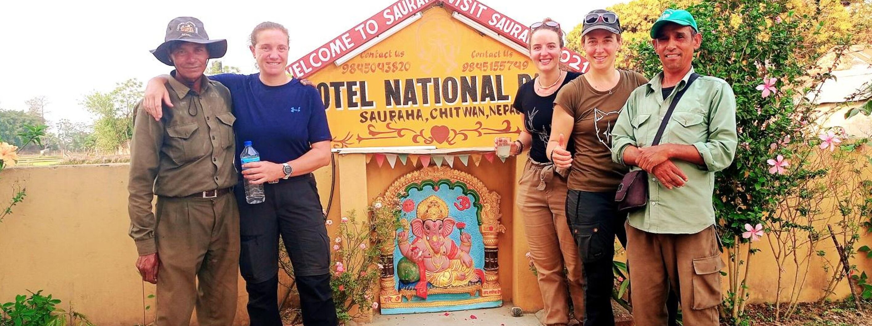 A group of people standing in front of a building labeled "Hotel National" with a traditional Indian architectural design and a deity statue.