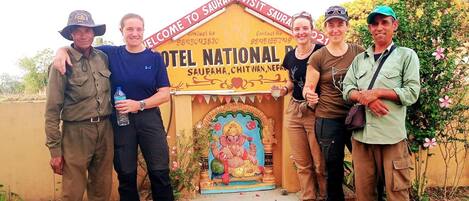 A group of people standing in front of a building labeled "Hotel National" with a traditional Indian architectural design and a deity statue.