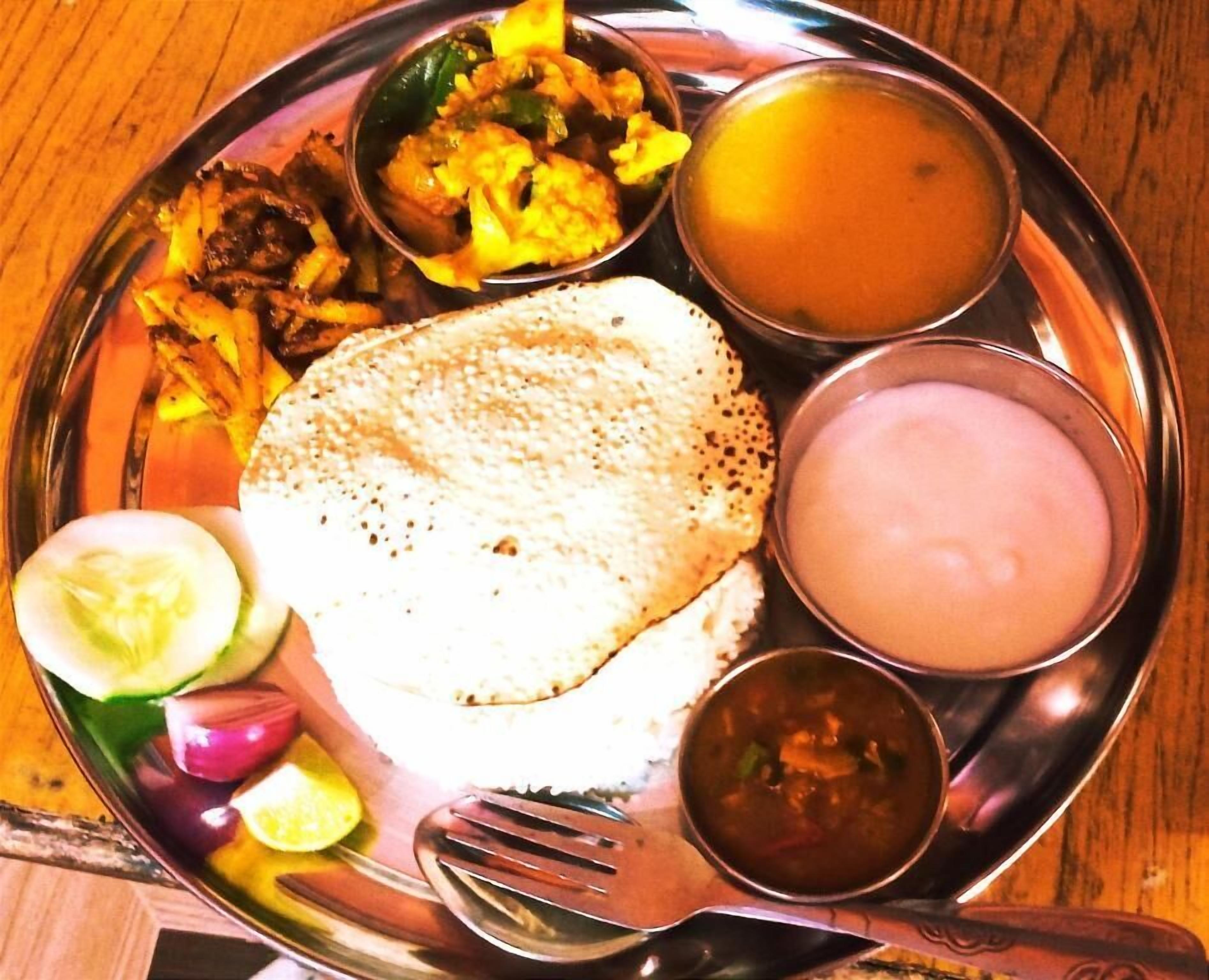 Un plato de acero inoxidable con varios platos de la cocina india, como pan plano, curry y dos tipos de sopa.