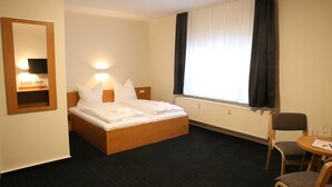 Een hotelkamer met een bed, een stoel, een tafel, een spiegel en een raam met gordijnen.