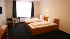 Een hotelkamer met twee bedden, een bureau, een stoel en een raam met gordijnen.