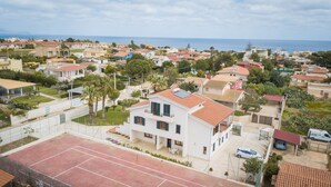 Een woonwijk met huizen, een tennisbaan en uitzicht op zee.
