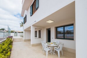 Une terrasse extérieure moderne, avec une table et des chaises blanches, un espace abrité doté d’une porte, et une vue sur le quartier environnant.