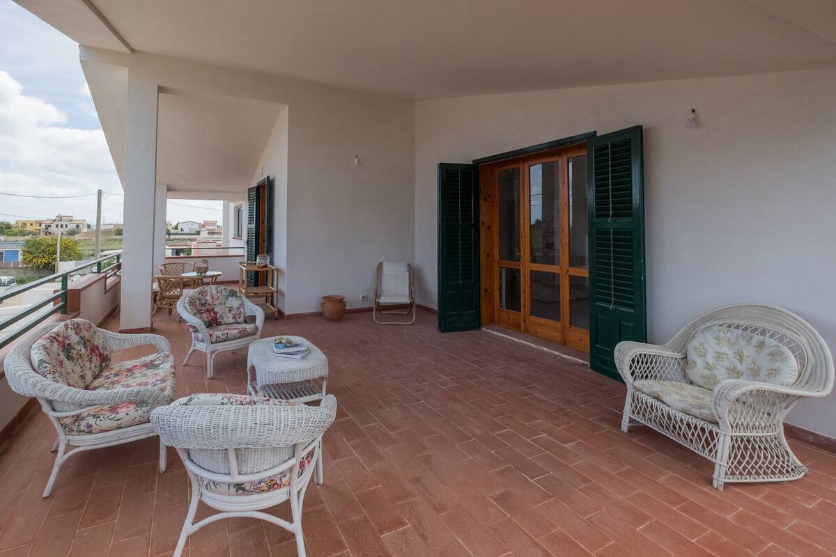 A balcony with wicker furniture, a wooden door, and a view of the surrounding area.