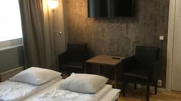 A hotel room with a bed, two chairs, a small table, a flat-screen TV mounted on the wall, and a window with curtains.
