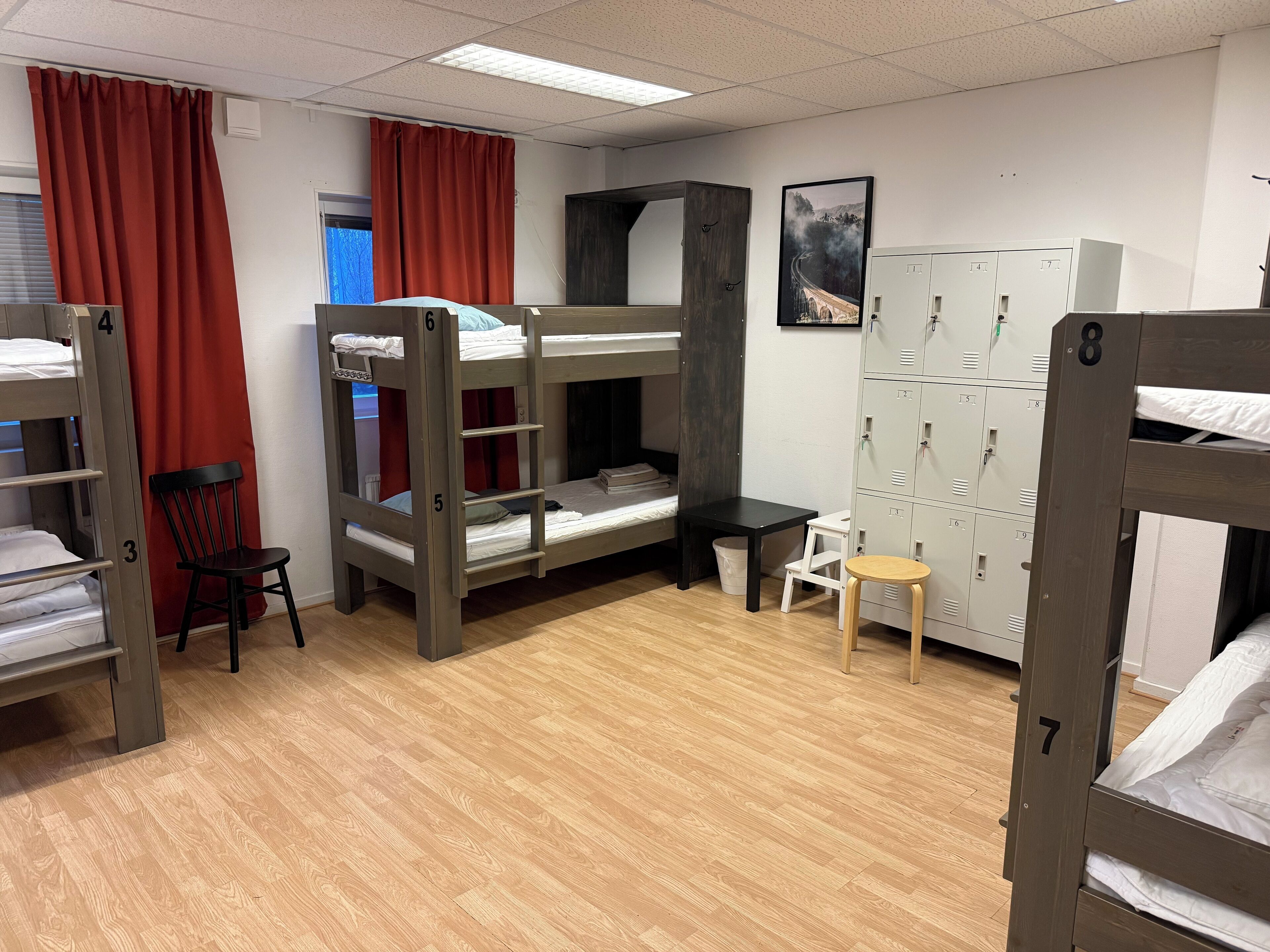 A dormitory room with bunk beds, a desk, a chair, and a set of lockers.