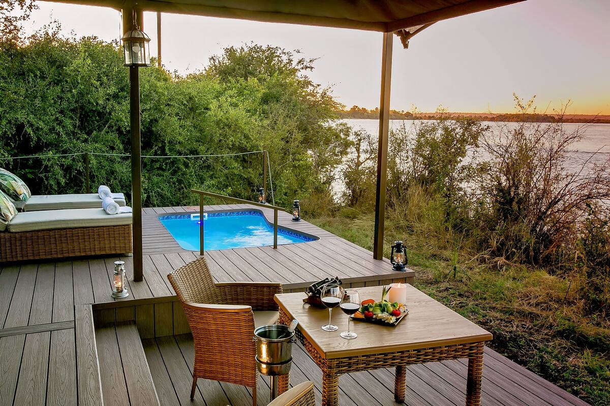 A wooden deck with a hot tub, wicker furniture, and a table set for dining with a view of the lake.