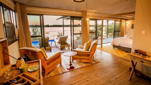 A room with a bed, a dining table, and a seating area with a view of a body of water.