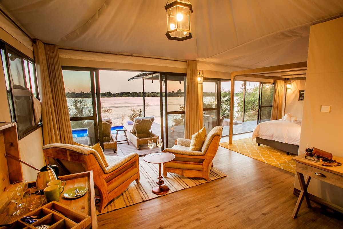 A room with a bed, a dining table, and a seating area with a view of a body of water.