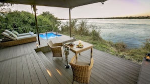 A wooden deck with a pool, wicker furniture, and a table set for dining.