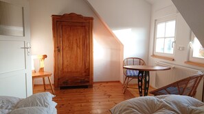 Ett mysigt sovrum på vinden med en trädörr, ett litet bord, en flätstol och en säng.