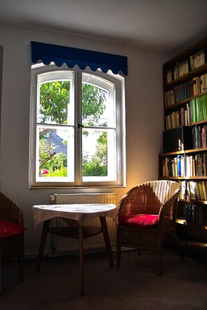 A room with a large window, a bookshelf, a wicker chair, and a table. - Altes Haus der Seefahrtschule Grünbaum Ostseebad-Wustrow (near Ahrenshoop) Darss (Ostseebad-Wustrow)