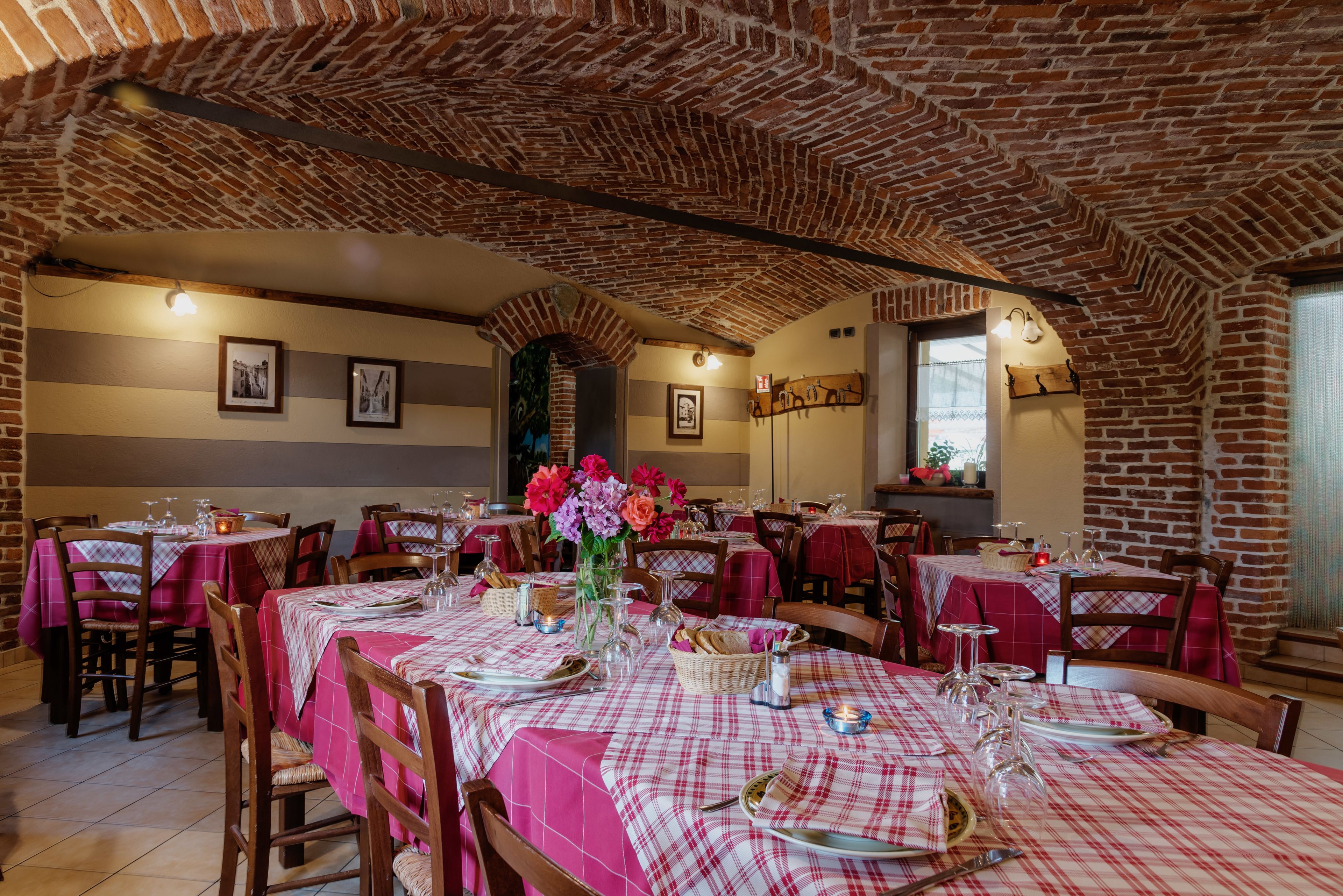A restaurant with brick walls and red and white checkered tablecloths. Tables are set with plates, glasses, and cutlery.