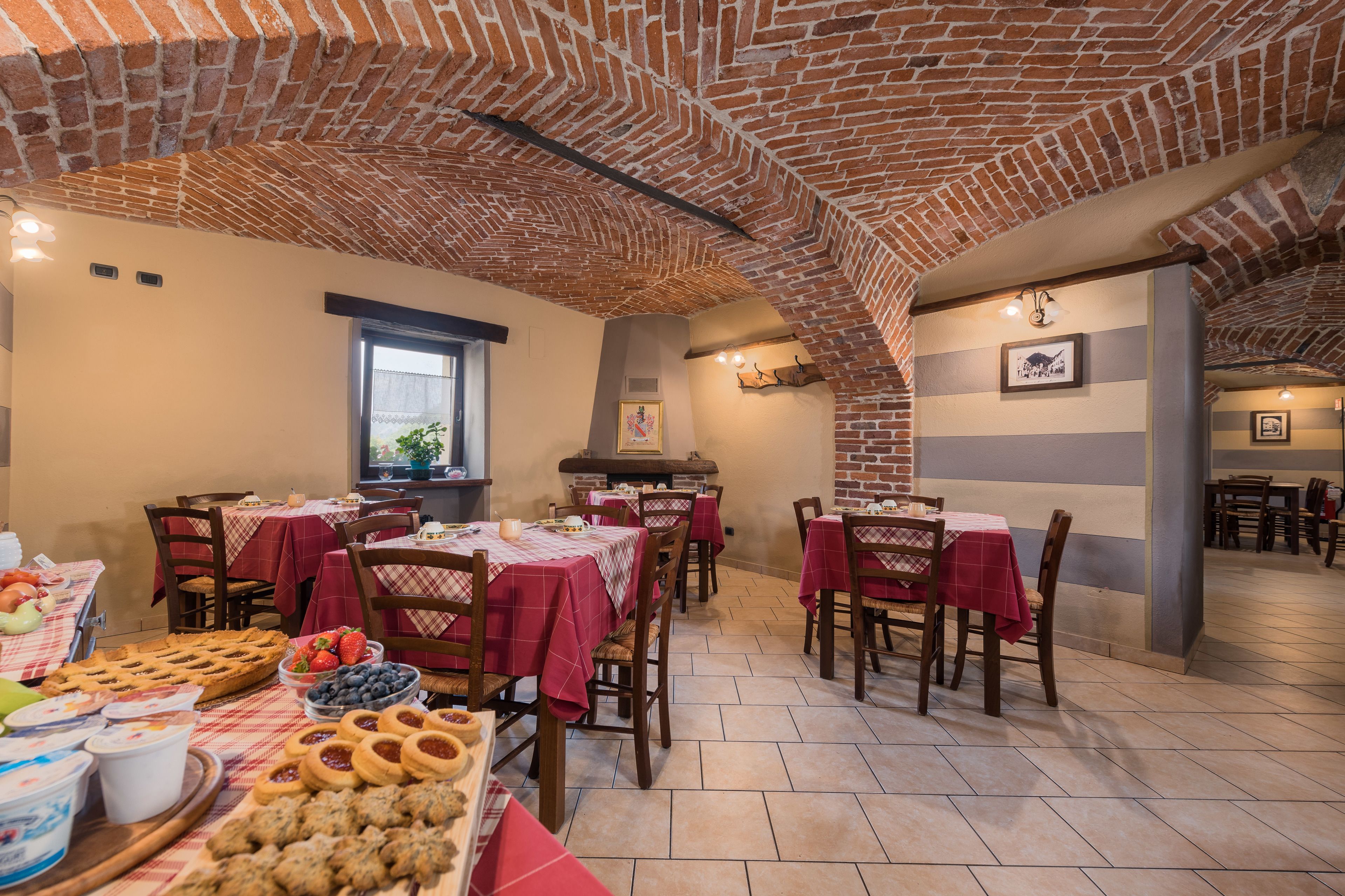 A dining area with brick ceiling, tables with red tablecloths, and various food items on the tables.