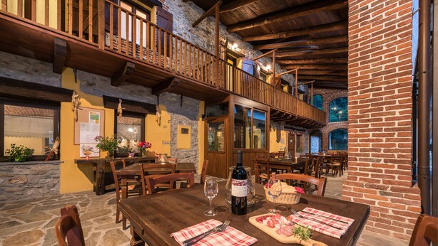 A rustic dining area with wooden tables, stone walls, and a balcony overlooking the interior. - Cascina Veja (Chiusa di Pesio)
