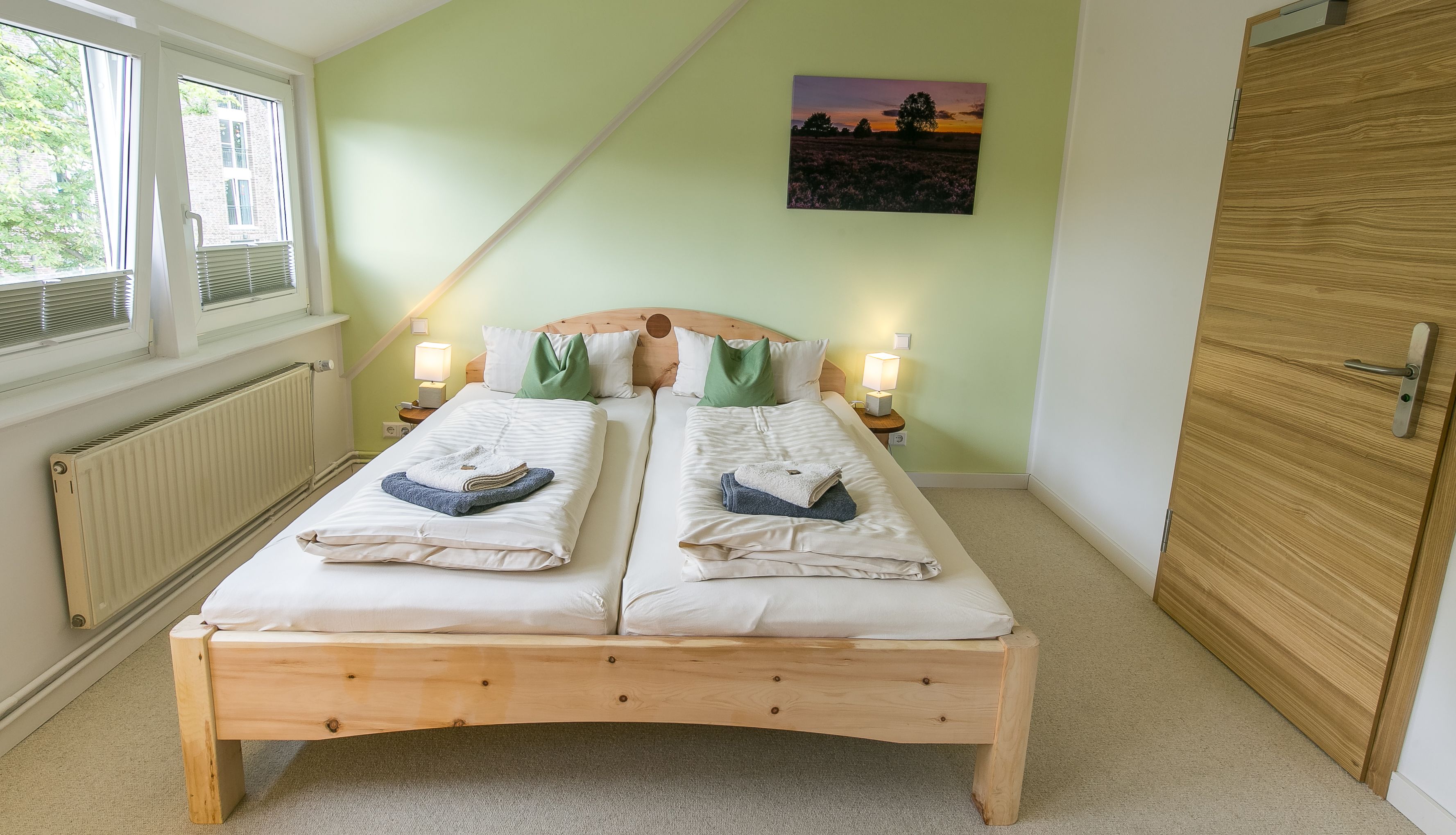 A double bed with two pillows, a nightstand with a lamp, a radiator, and a wooden door.