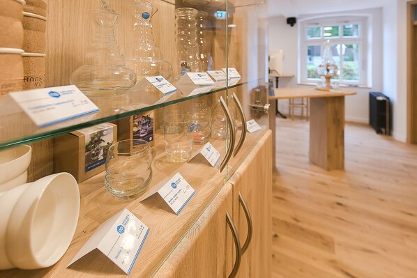 Cristalería transparente exhibida sobre una encimera de madera con etiquetas, un suelo de madera y una ventana al fondo.