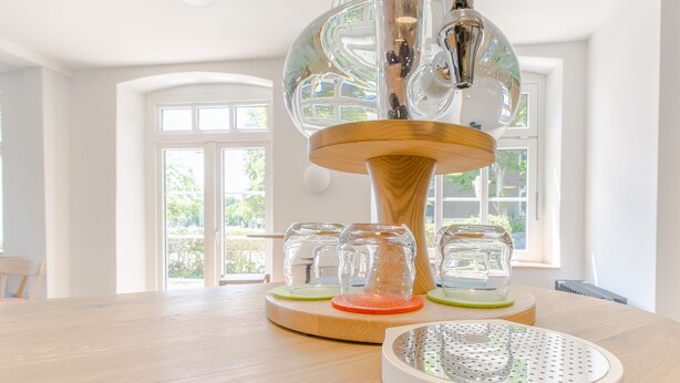 Una cocina moderna con una mesa de madera, una cafetera de vidrio y una jarra para café sobre un pedestal de madera.