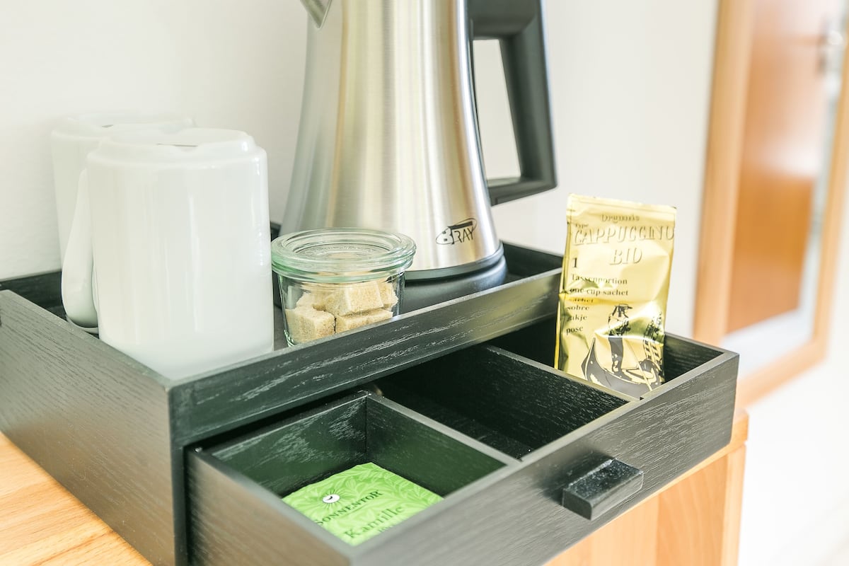 A kitchen area with a coffee maker, a glass jar with sugar cubes, a packet of instant coffee, and a green tea sachet.