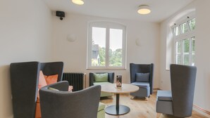 Un área de estar moderna con sillones tapizados de gris, una mesa redonda de madera y un amplio ventanal que proporciona luz natural.